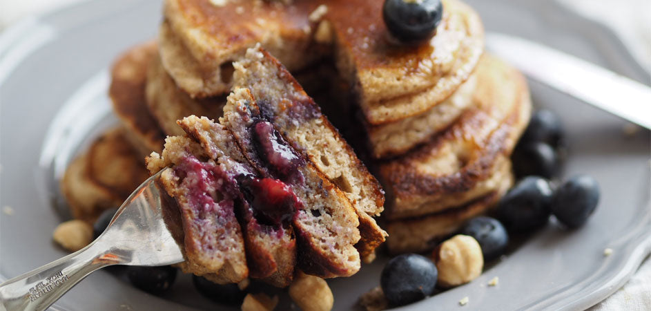 Frisch gebackene Pancakes mit Heidelbeeren, gestapelt auf einem Teller, garniert mit Sirup und frischen Beeren – ein gesunder, proteinreicher Start in den Tag.