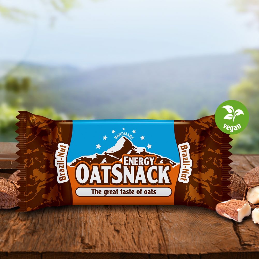 Davina Oatsnack Brazil Nut auf einem Holztisch, umgeben von Nüssen, mit natürlicher Landschaft im Hintergrund.