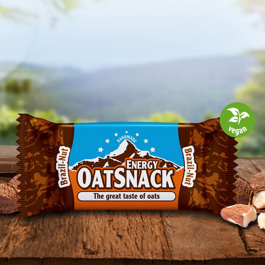 Davina Oatsnack Brazil Nut auf einem Holztisch, umgeben von Nüssen, mit natürlicher Landschaft im Hintergrund.