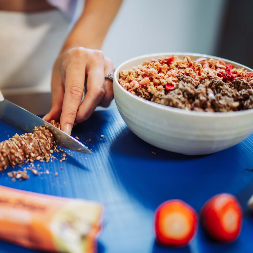Protein Delight Riegel von Multipower neben Müsli-Bowl mit Früchten, Riegelstücke als Topping in der Schale.
