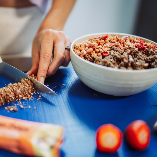 Protein Delight Riegel von Multipower neben Müsli-Bowl mit Früchten, Riegelstücke als Topping in der Schale.