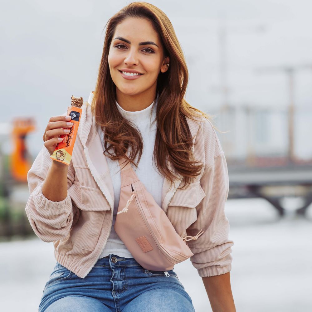 Frau hält einen geöffneten Multipower Protein Delight Riegel in der Hand – ready-to-eat Moment für bewussten Snackgenuss unterwegs.