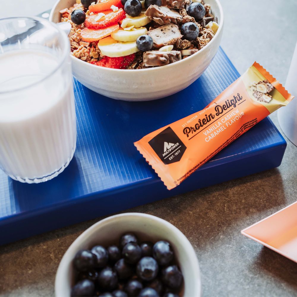 Multipower Protein Delight Riegel neben einer Bowl mit Müsli und frischen Früchten – Teile des Riegels wurden in die Bowl geschnitten und integriert, als kreativer Protein-Topping.