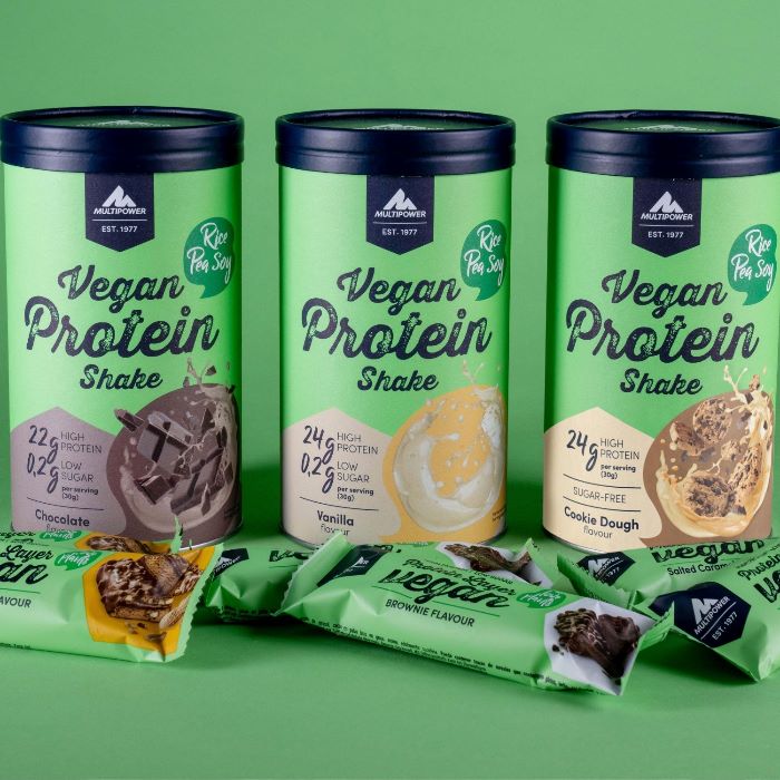 Alle Sorten des Multipower Vegan Protein Shake 420g auf grünem Hintergrund – davor platzierte Vegan Layer Protein Riegel als idealer pflanzlicher Begleiter.
