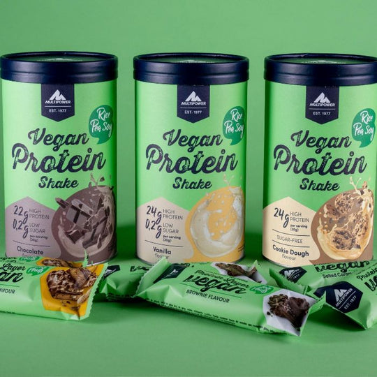 Alle Sorten des Multipower Vegan Protein Shake 420g auf grünem Hintergrund – davor platzierte Vegan Layer Protein Riegel als idealer pflanzlicher Begleiter.